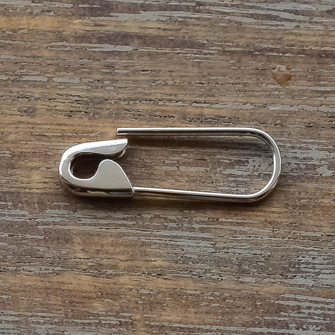 3/4 inches white gold safety pin earring on a wooden surface