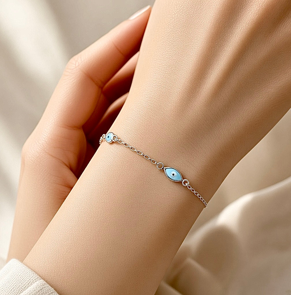 Sterling silver chain bracelet with a small blue evil eye charm and dainty heart accent.