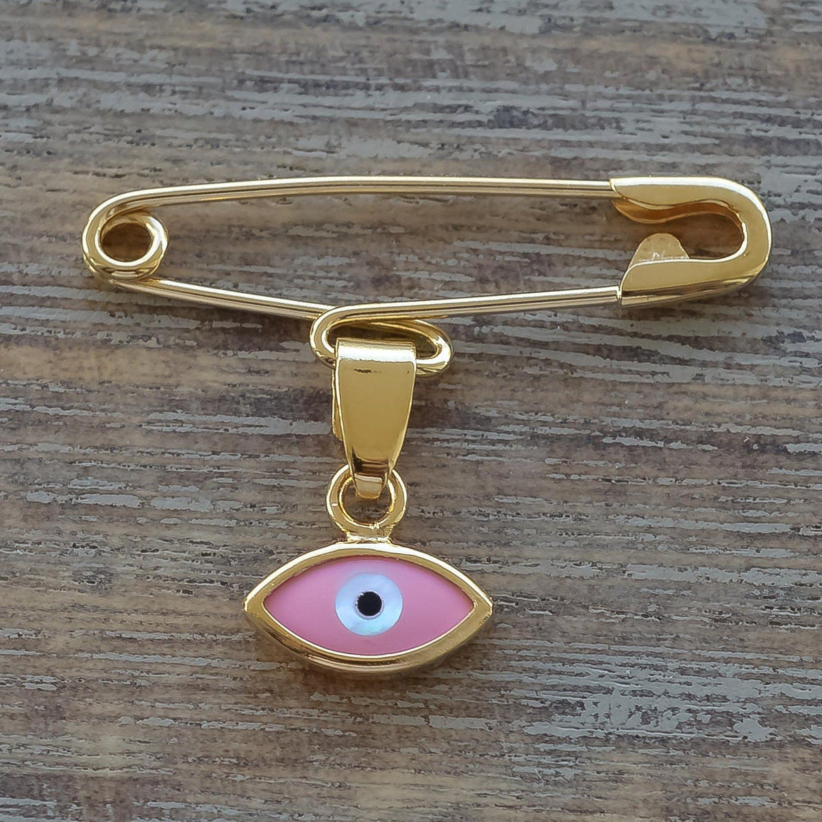 14K Gold Baptism Baby Pin Pink Evil Eye Brooch on wooden surface