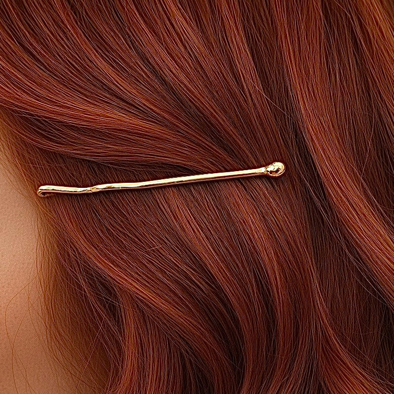 Thin gold bobby pin with rounded end securing rich auburn hair strands.