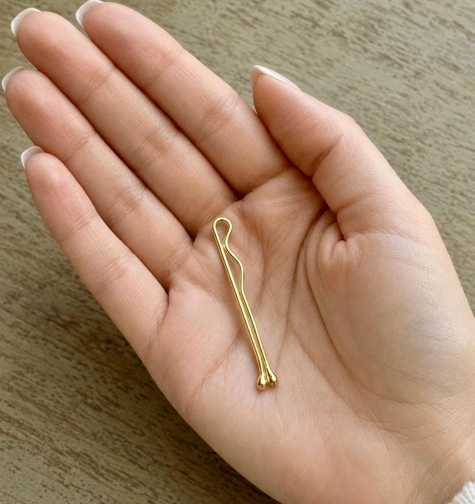 Delicate 14K yellow gold bobby pin with rounded ends held in a woman's hand on wood background.