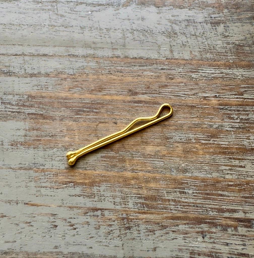 Minimalist solid 14K yellow gold bobby pin with smooth finish on textured wooden surface.