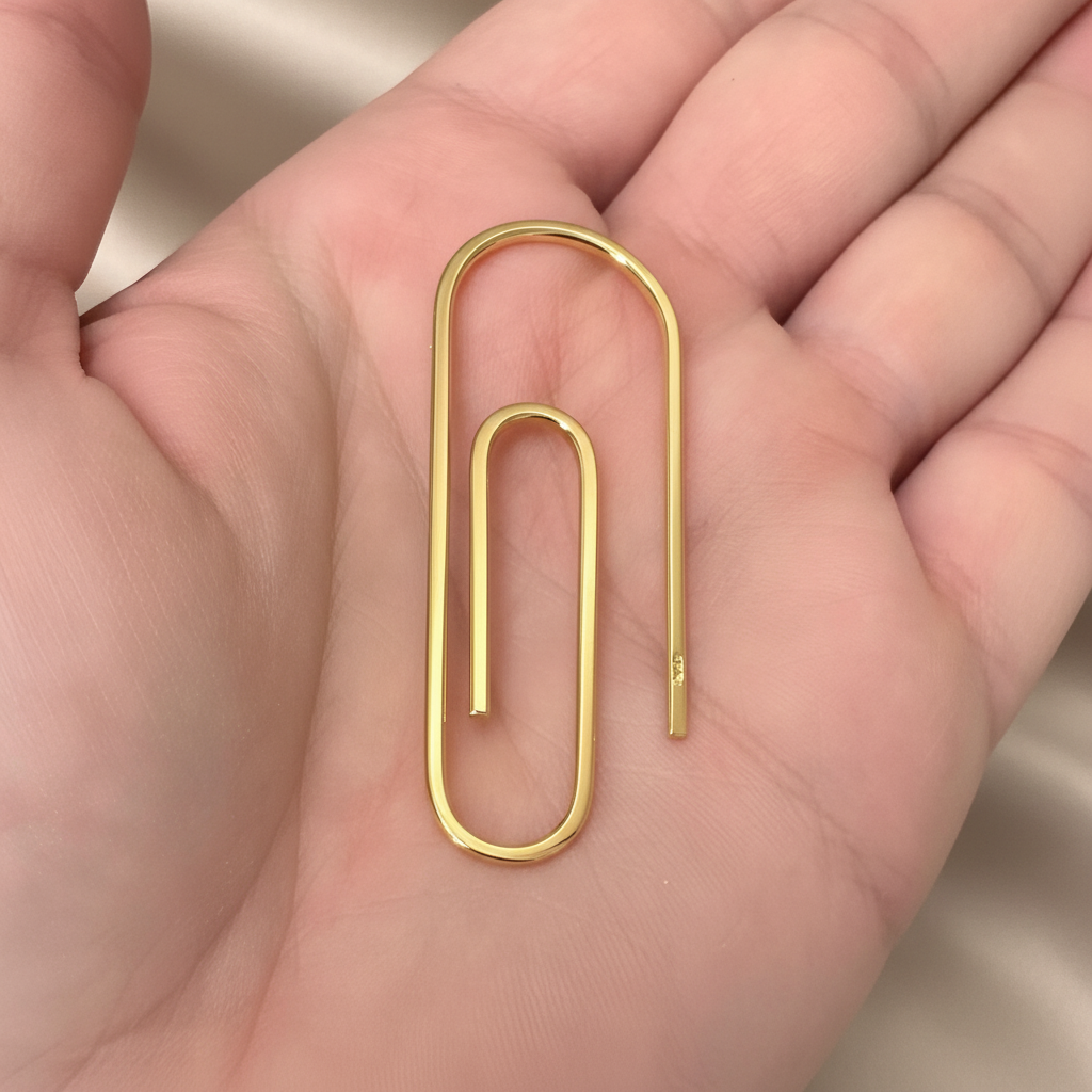 Handcrafted gold-tone metal money clip shaped like an oversized paperclip held in hand.