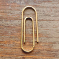 Handcrafted gold paperclip money clip with smooth polished finish on wooden surface.