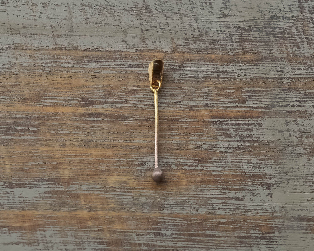 Gold-plated sterling silver pendant shaped like a minimalist matchstick on a wooden surface.
