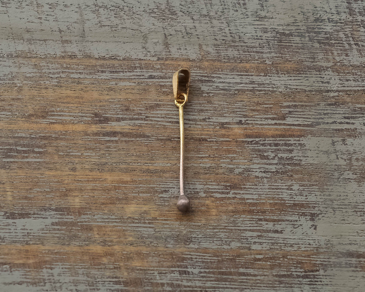 Gold-plated sterling silver pendant shaped like a minimalist matchstick on a wooden surface.
