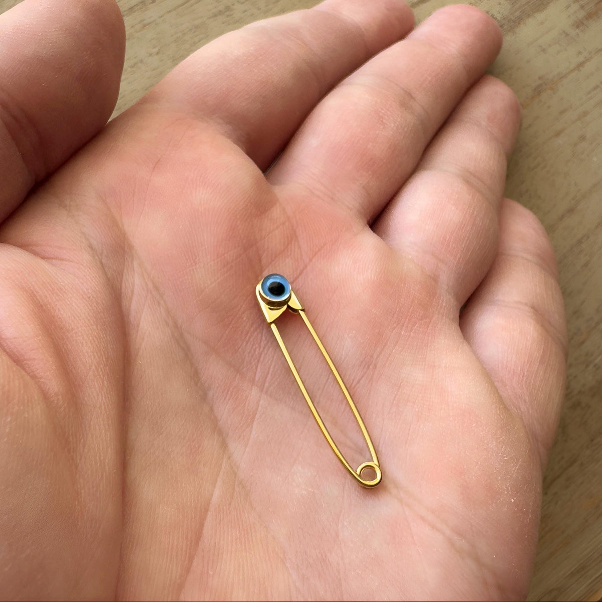 Sterling Silver Safety Pin Evil Eye Baby Protection Brooch Gold Plated held in a hand - 24jewels