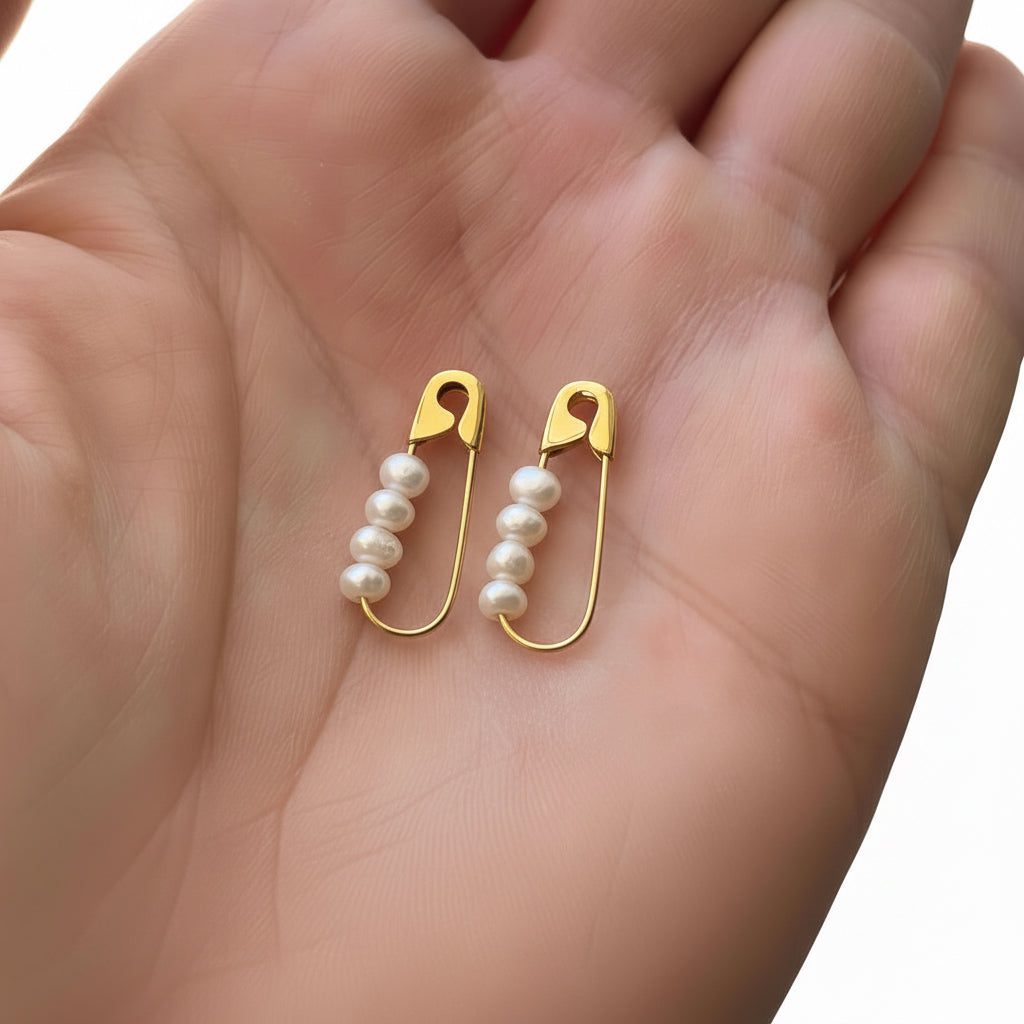 Gold-plated safety pin silver earrings with four small white pearls on each pin, held in palm.