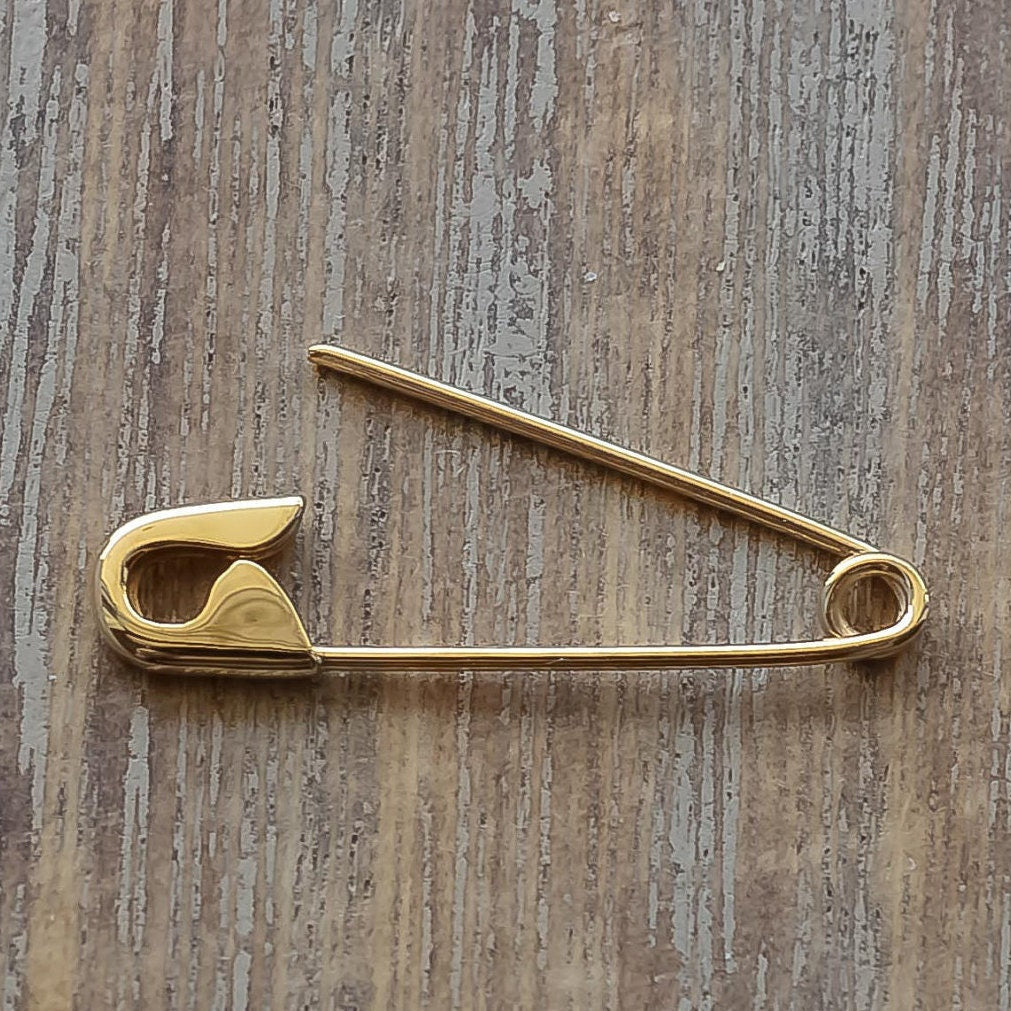 Gold safety pin earring with a sleek, minimalist design on a wooden background.