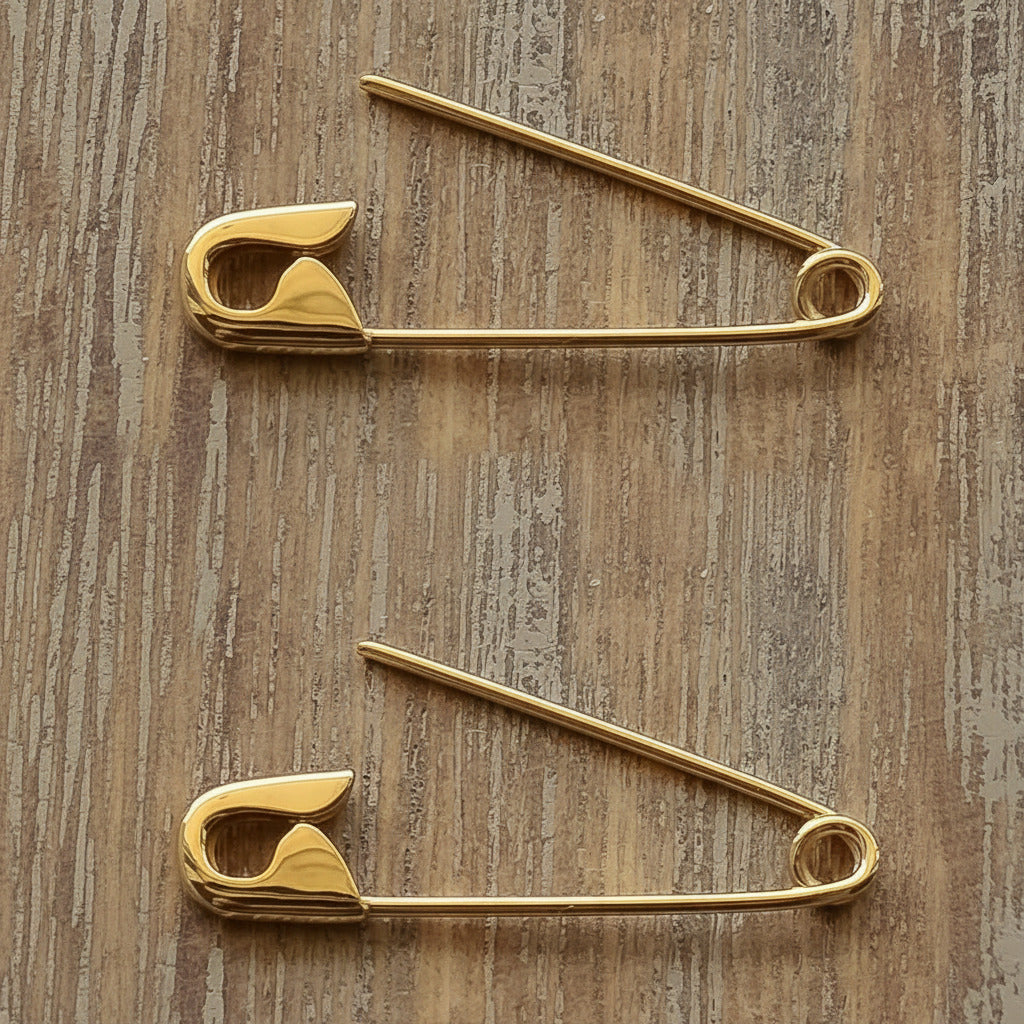Pair of 1-inch gold safety pin earrings with smooth, polished finish on wood surface.