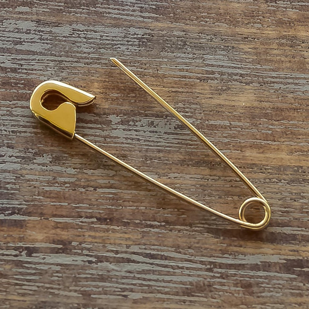 Minimalist gold safety pin earring with smooth, polished finish on wooden surface.