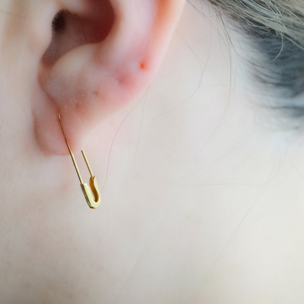 1-inch gold safety pin hoop earring worn on ear, sleek and minimalist design.
