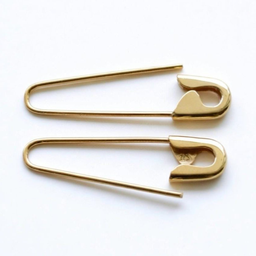 Pair of shiny gold safety pin hoop earrings with smooth curved edges on a white background.