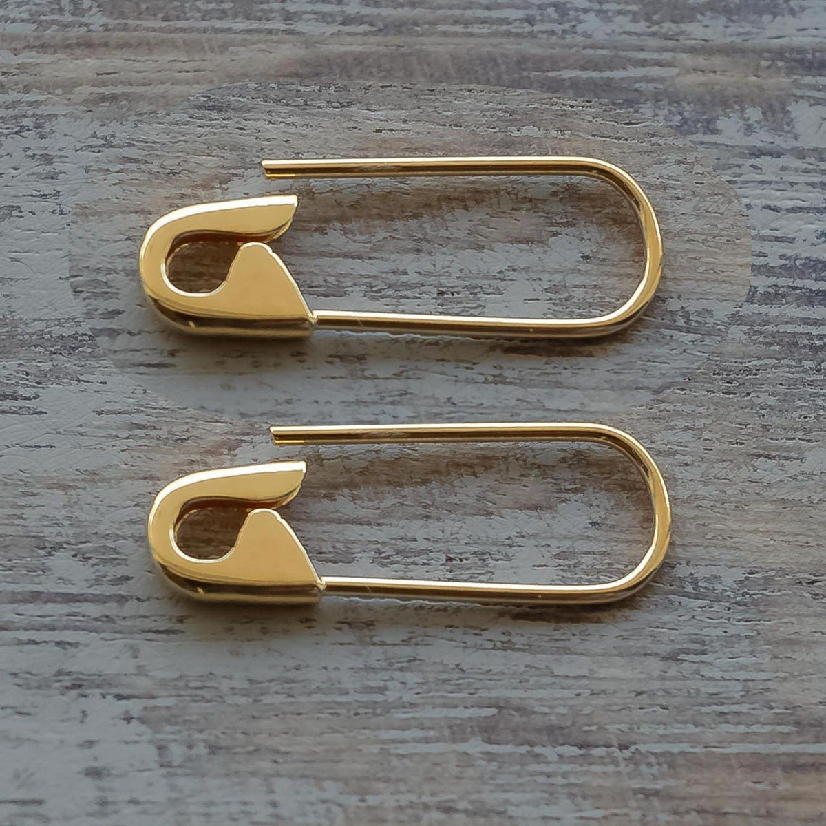 Pair of 3/4” gold safety pin hoop earrings with smooth, shiny finish on wood surface.