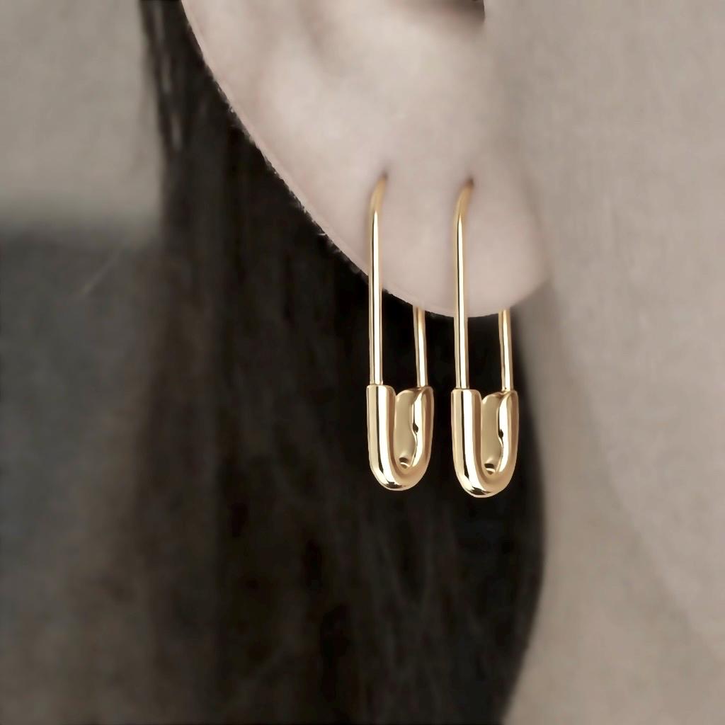 yellow gold hoop earrings designed as small safety pins, minimalist style worn on earlobe . 