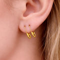 Small gold safety pin hoop earrings worn on pierced earlobe, minimalist punk style.