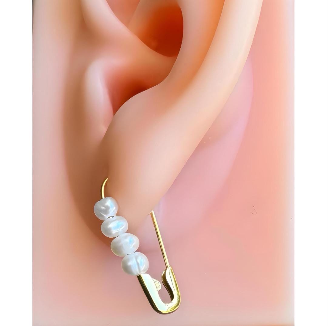 Gold safety pin hoop earring with four freshwater pearls on a 3/4-inch curved design on ear .