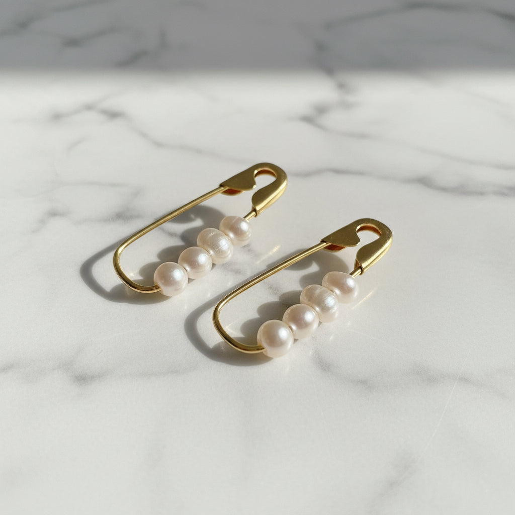 Gold safety pin earrings with four white freshwater pearls on each pin on a marble surface .
