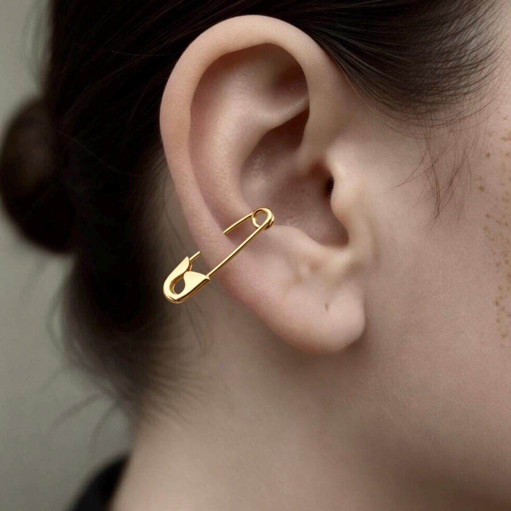 Small gold safety pin earring worn on the ear, minimalist punk style jewelry.