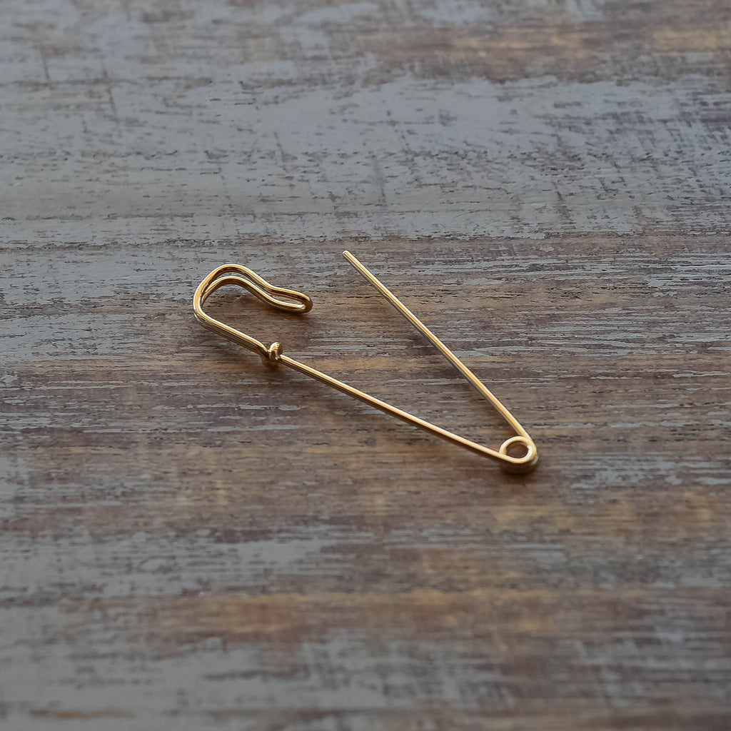 Delicate gold safety pin wire earring with minimalist, polished finish on wood surface.