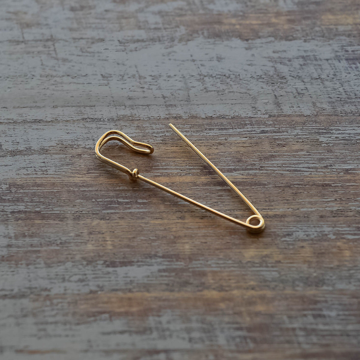 Delicate gold safety pin wire earring with minimalist, polished finish on wood surface.