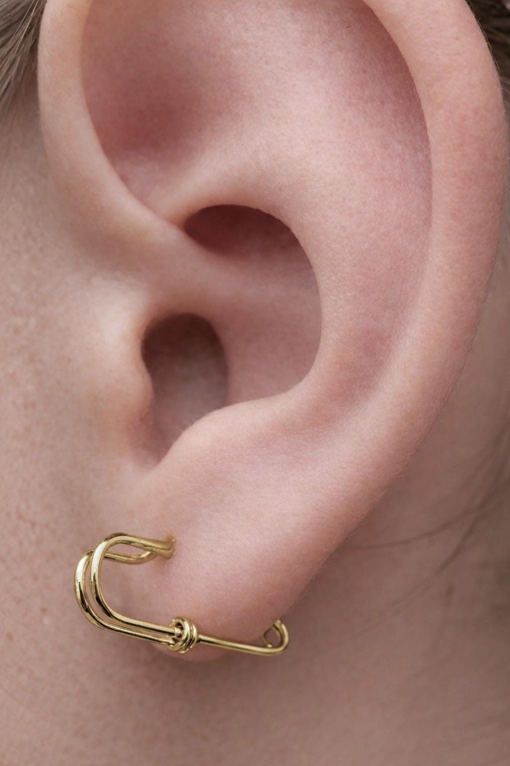 Small gold safety pin earring with minimalist wire design in ear lobe.
