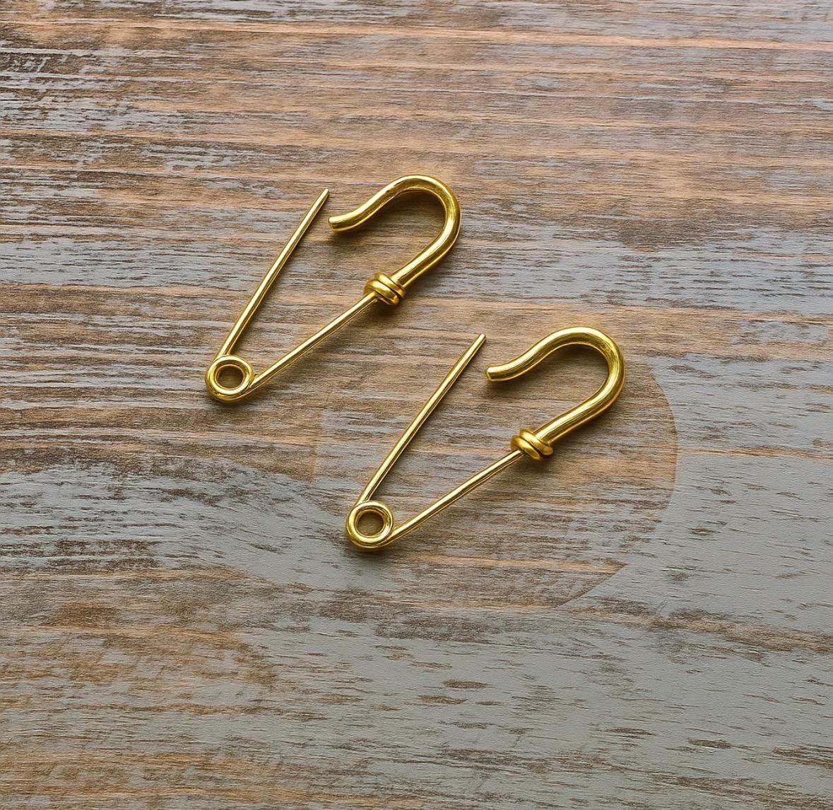 Pair of small gold safety pin wire earrings with a minimalist edgy design on wood background.
