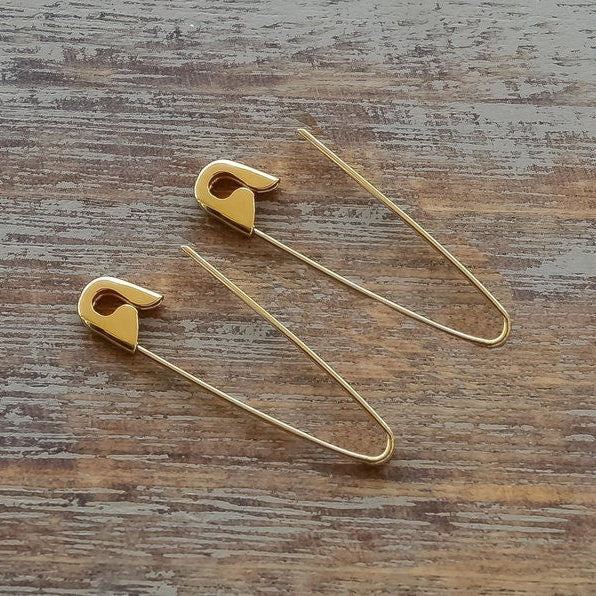 Gold plated safety pin hoop earrings with a sleek, minimalist design, 1.25 inches long on wooden surface .
