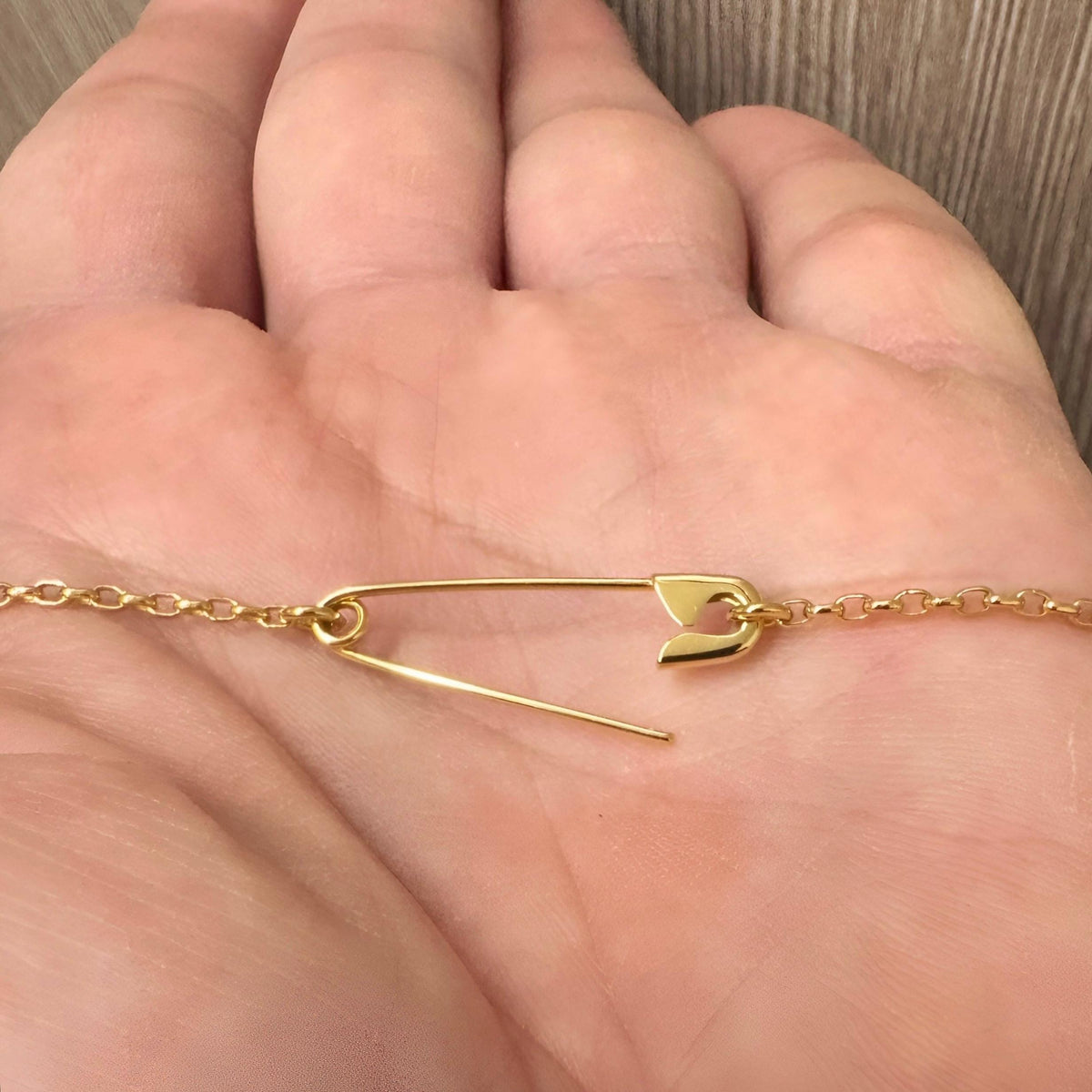 Gold-plated safety pin necklace with delicate chain resting on a hand.