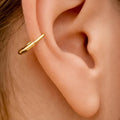 Small polished gold hoop earring with safety pin design worn on outer ear cartilage.