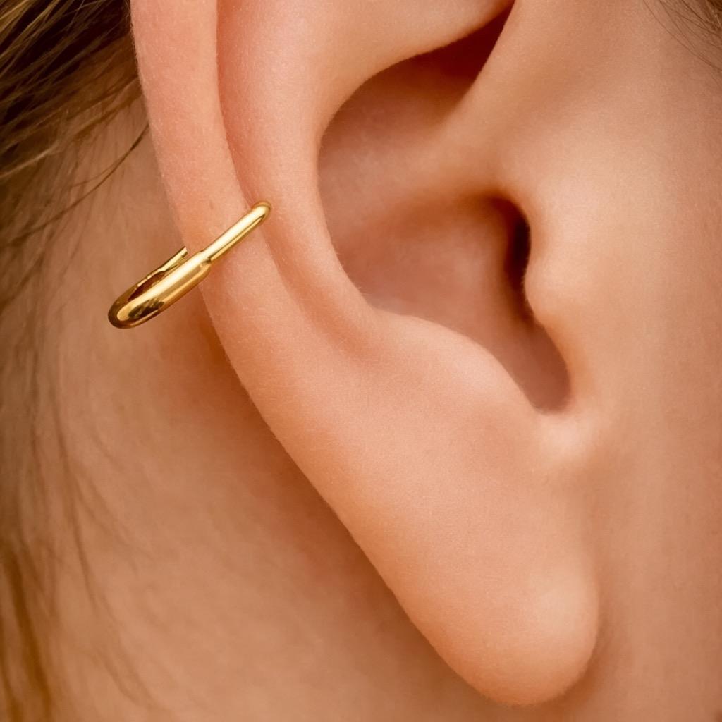 Small polished gold hoop earring with safety pin design worn on outer ear cartilage.