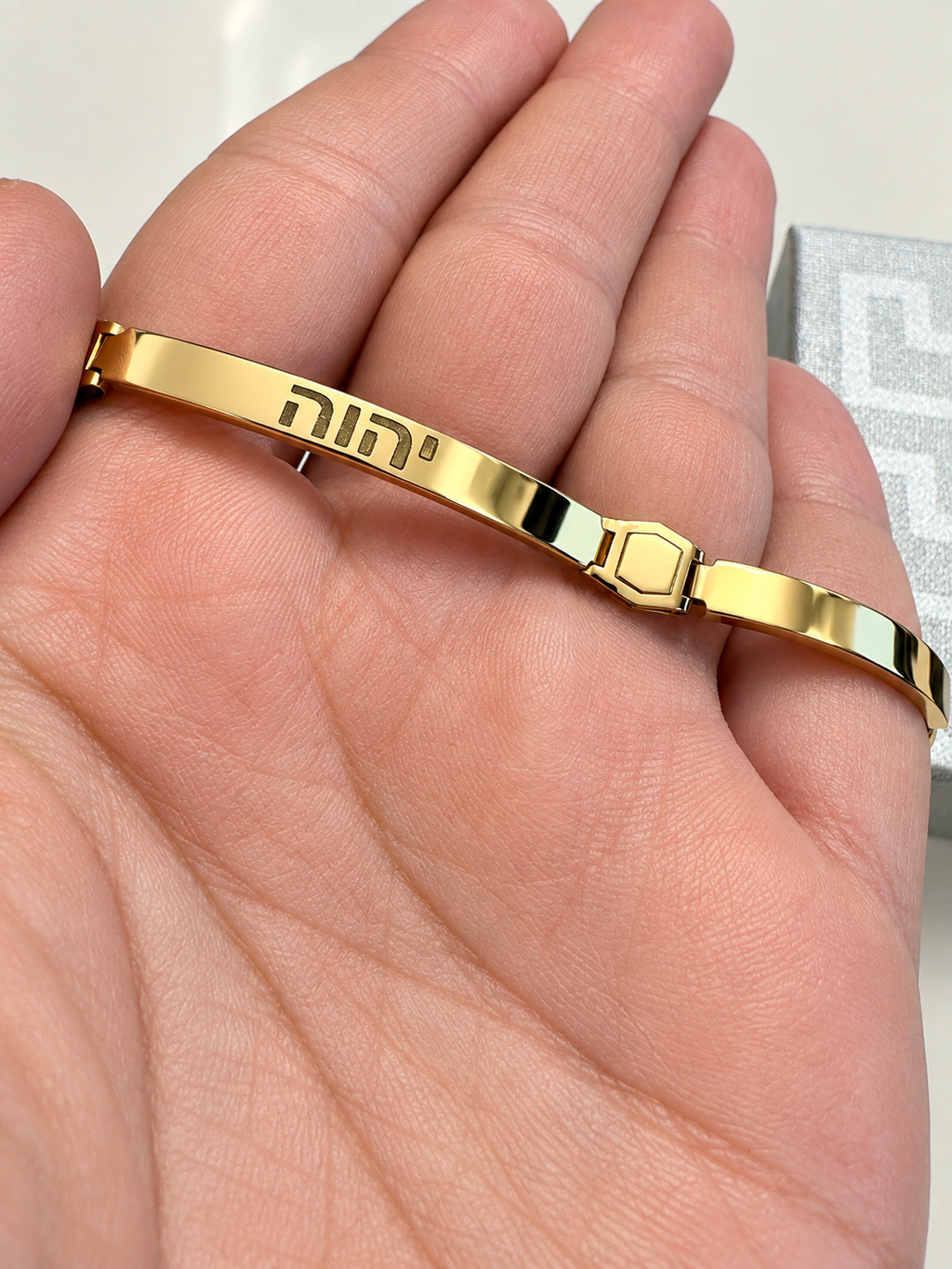 Gold plated sterling silver men's bracelet with engraved Hebrew letters and smooth polished finish held in a palm .