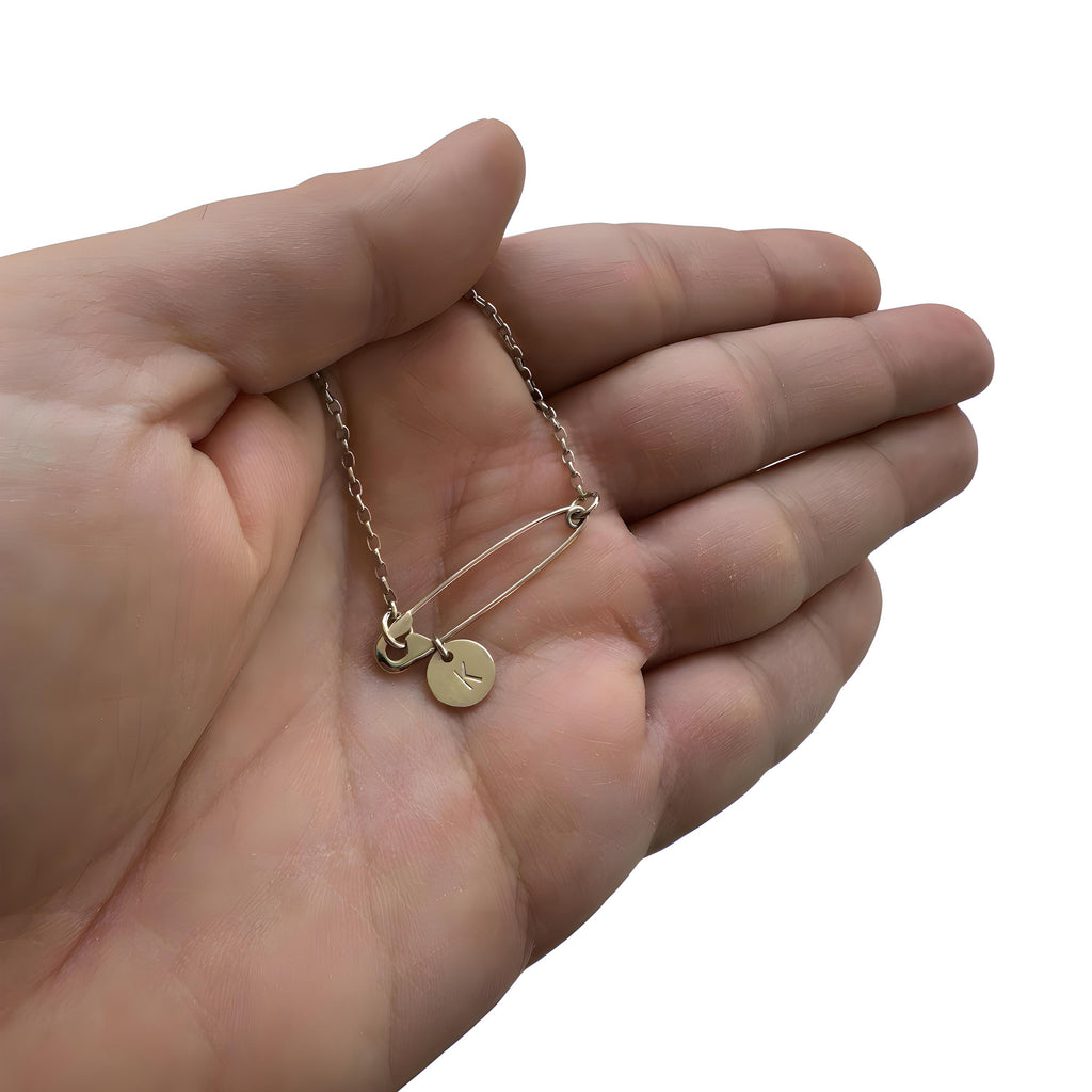 Sterling silver safety pin necklace with small round initial charm on delicate chain held in hand.