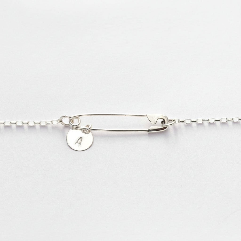 Sterling silver safety pin necklace with round initial "A" charm on delicate chain on white background.