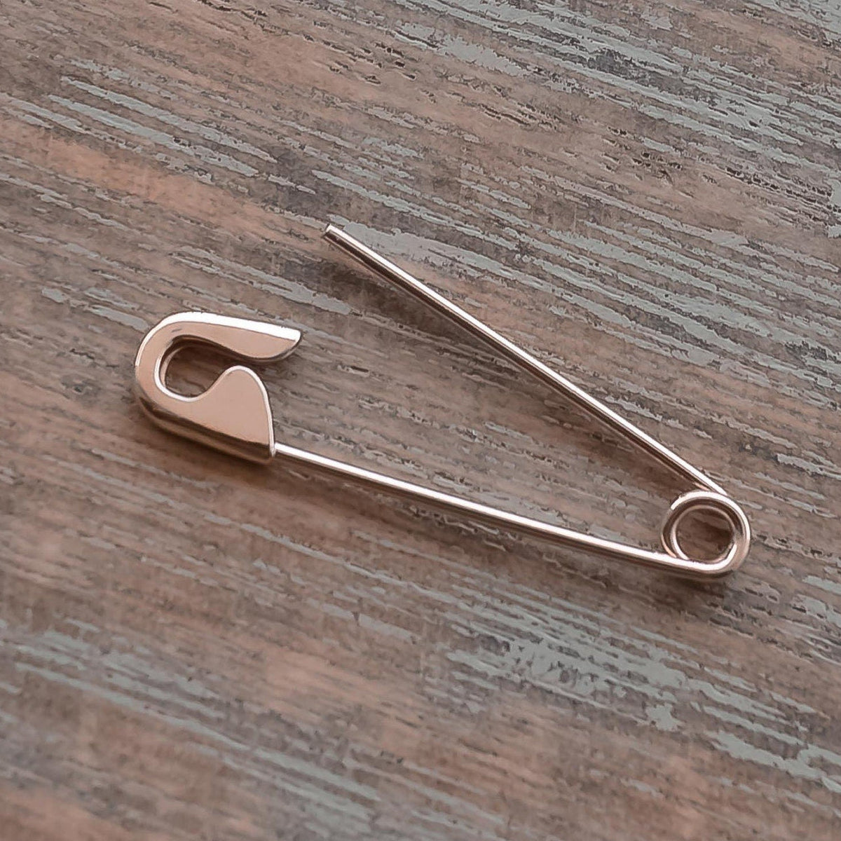 rose gold safety pin earring with sleek, minimalist design on wooden surface.