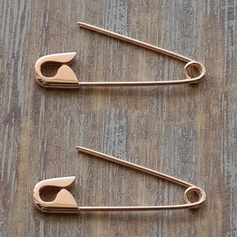 Pair of rose gold safety pin cartilage earrings with smooth polished finish on wooden surface.
