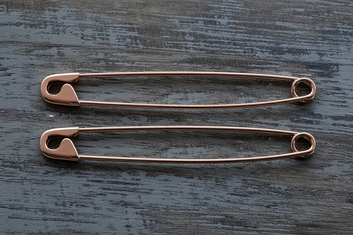 Pair of long rose gold safety pin earrings with a minimalist, sleek design  on wooden surface, 1.75-inch length.