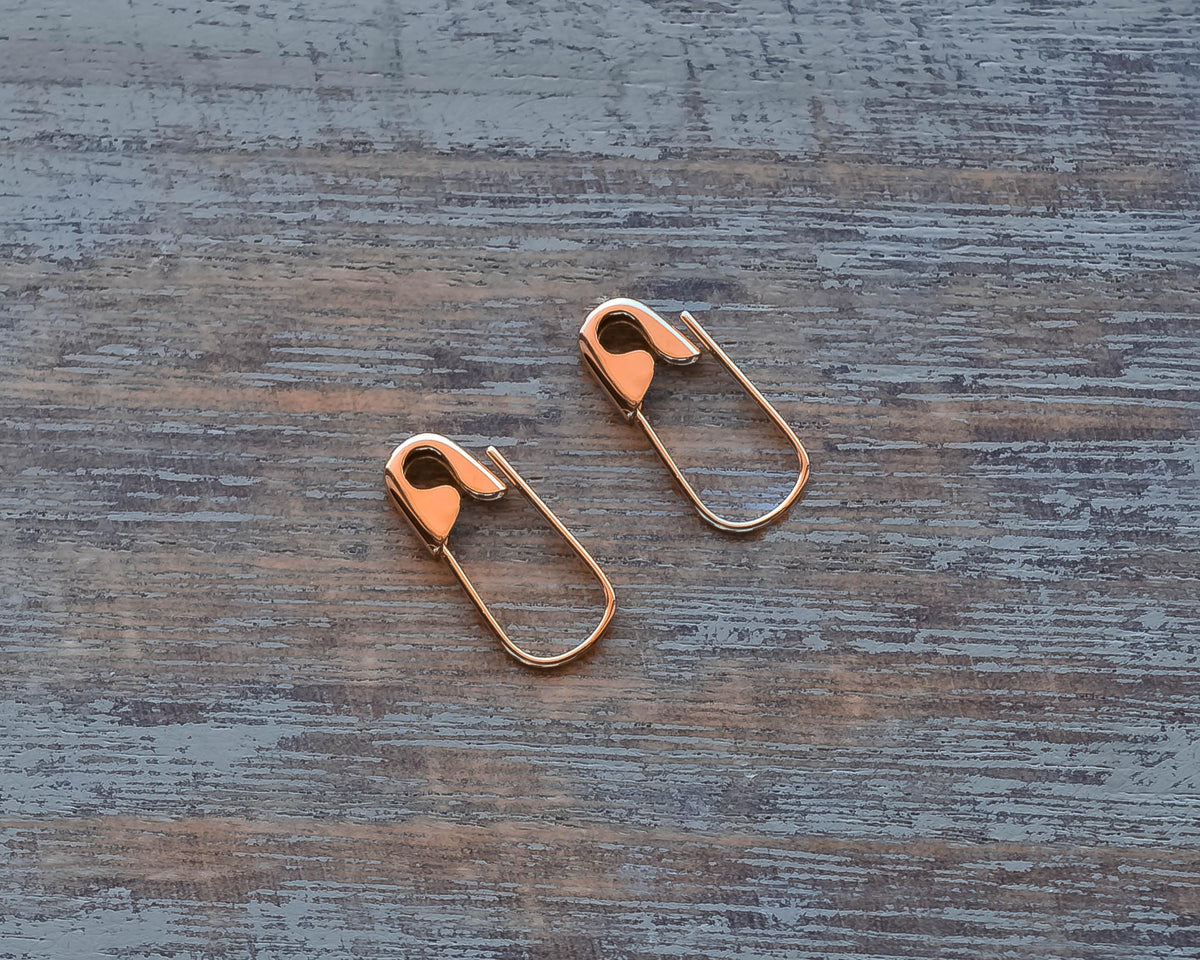 Pair of small rose gold hoop earrings with safety pin design, on wooden surface  measuring 5/8 inch each.