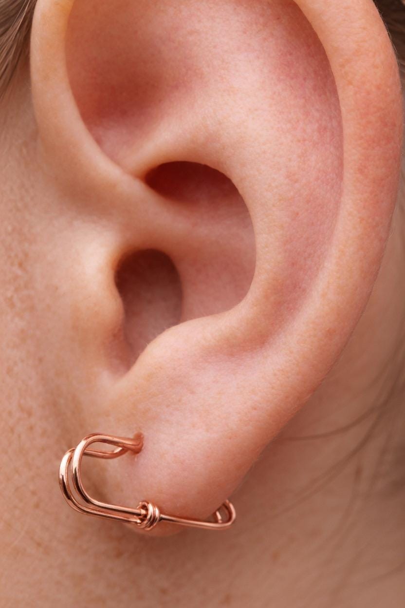 Small rose gold safety pin wire earring hooked on ear cartilage with minimal edgy style.
