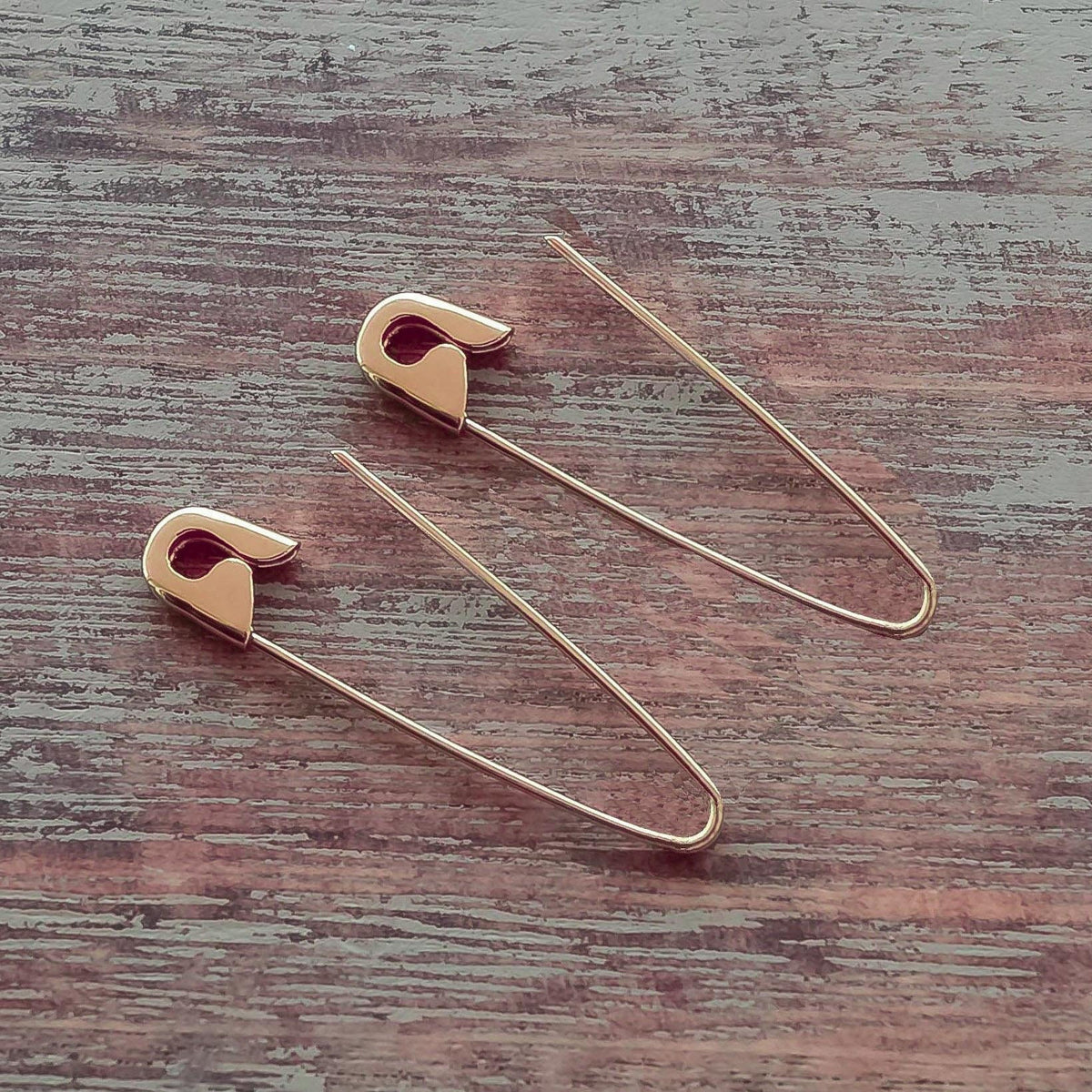 Rose Gold safety pin hoop earrings measuring 1.25 inches with a polished finish and sleek on wooden surface, minimalist design.