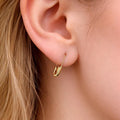 Gold safety pin mini hoop earring worn on earlobe, delicate punk-inspired design.