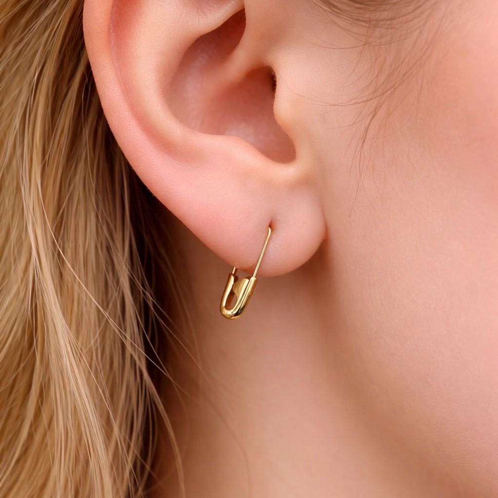 Gold safety pin mini hoop earring worn on earlobe, delicate punk-inspired design.