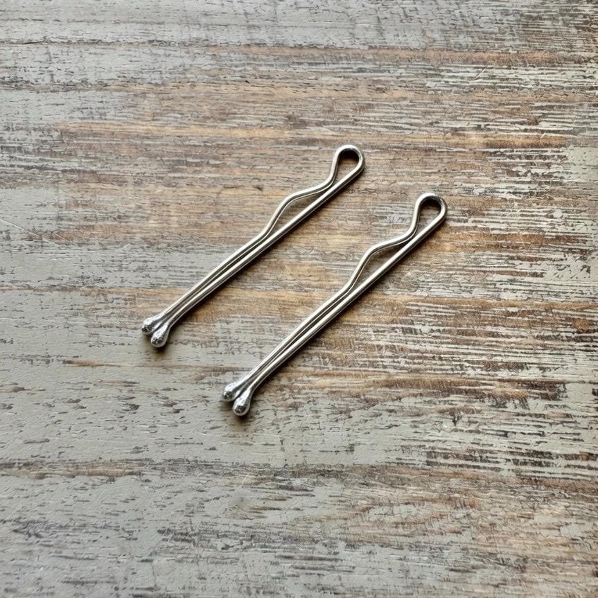 Two slender sterling silver bobby pins with minimalist looped ends on a textured wooden surface.