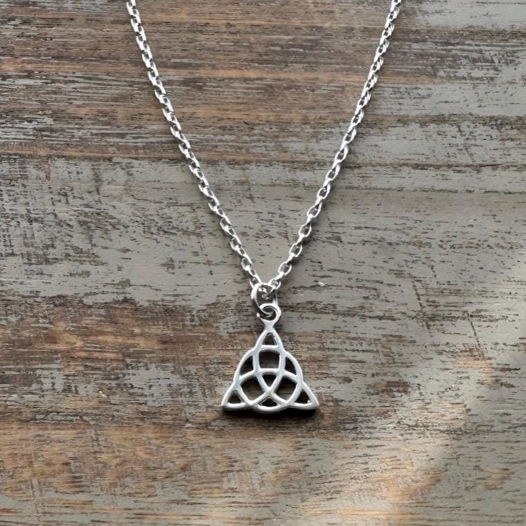 Sterling silver necklace with a minimalist Celtic triquetra knot pendant on a fine chain on wooden background .