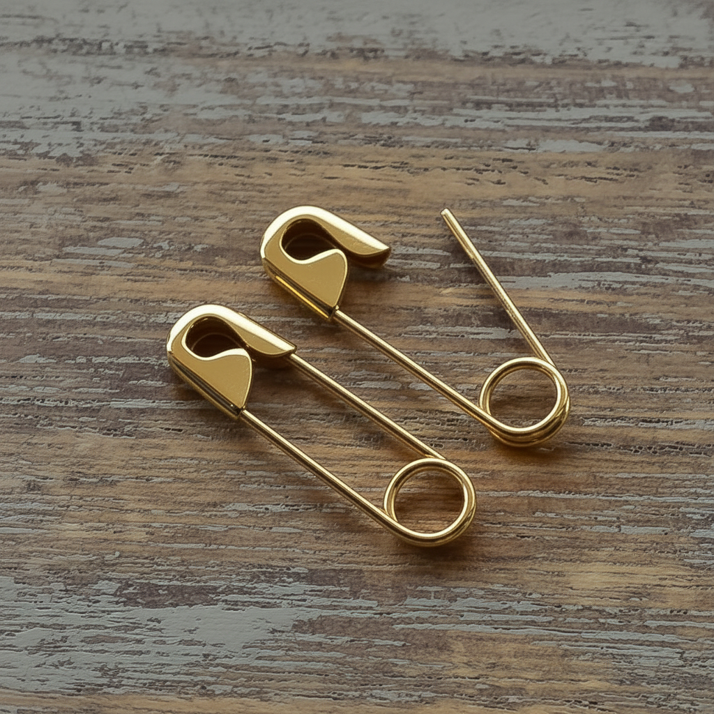 Gold-plated safety pin earrings with polished finish on a wooden surface.