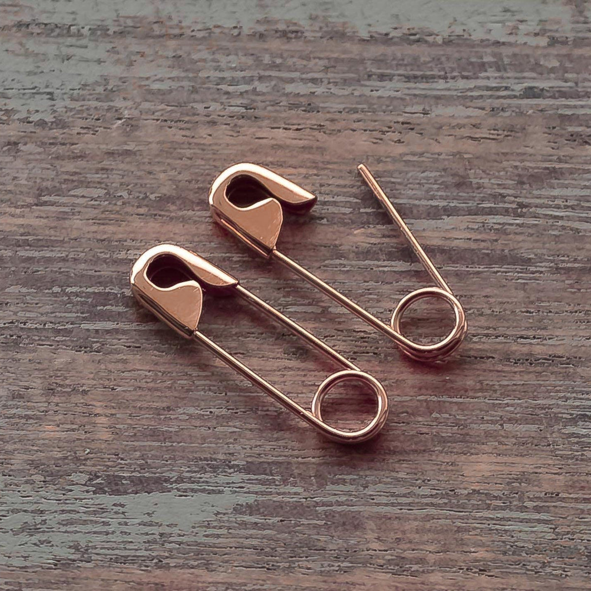 Pair of rose gold plated safety pin earrings with a polished finish on wood surface.