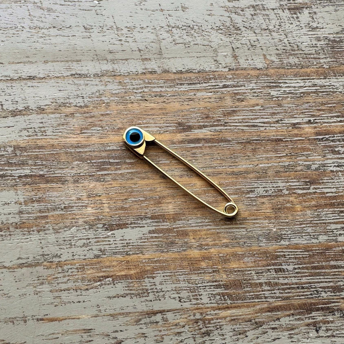 Sterling Silver Safety Pin Evil Eye Baby Protection Brooch Gold Plated on a wooden surface - 24jewels