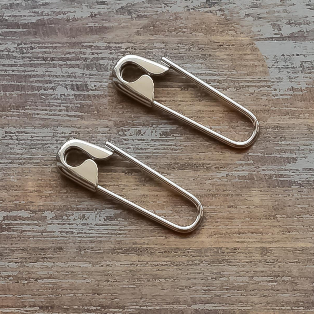 Sterling silver 3/4'' safety pin hoop earrings on rustic wooden surface.