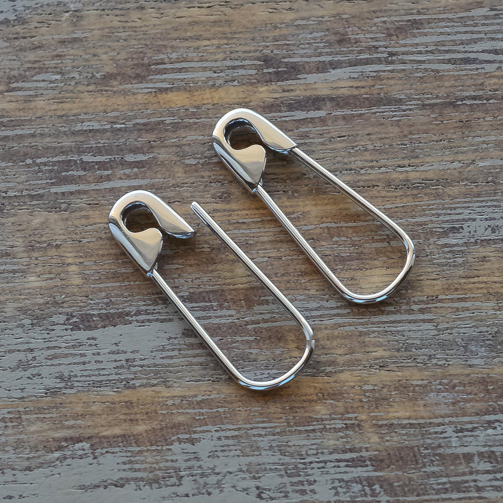 Sterling silver safety pin hoop earrings with a smooth polished finish on wooden surface.