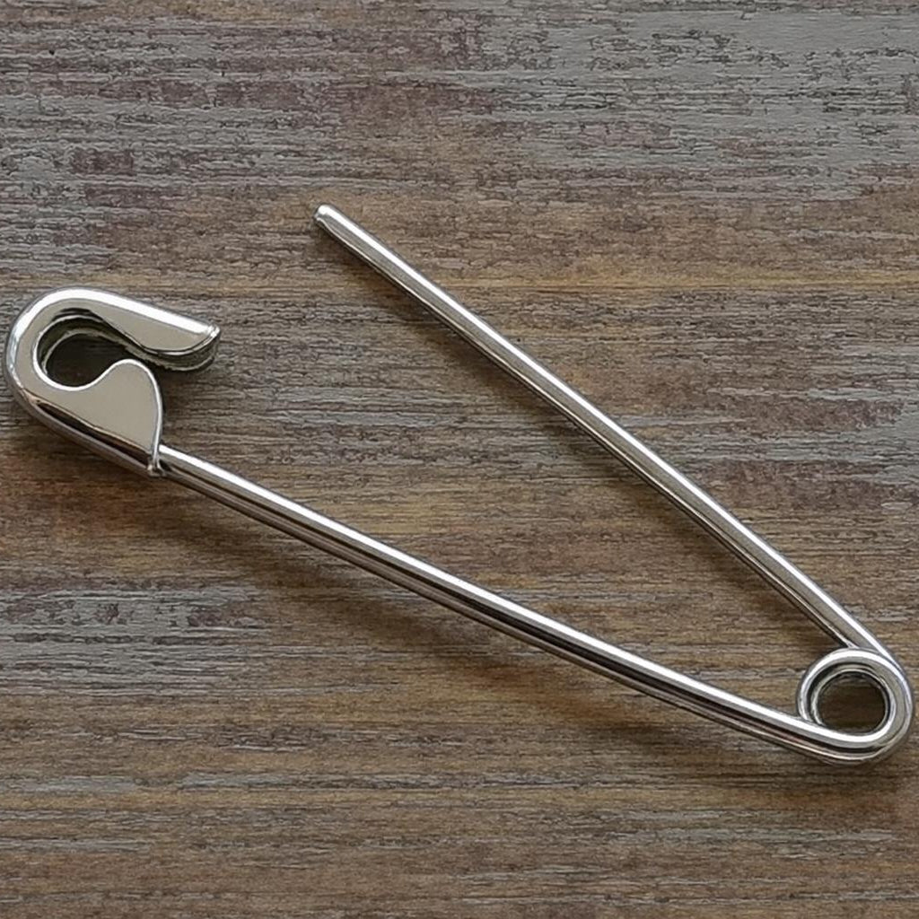 Sterling silver safety pin earring 1.3" long with 16 gauge thickness on wood surface.